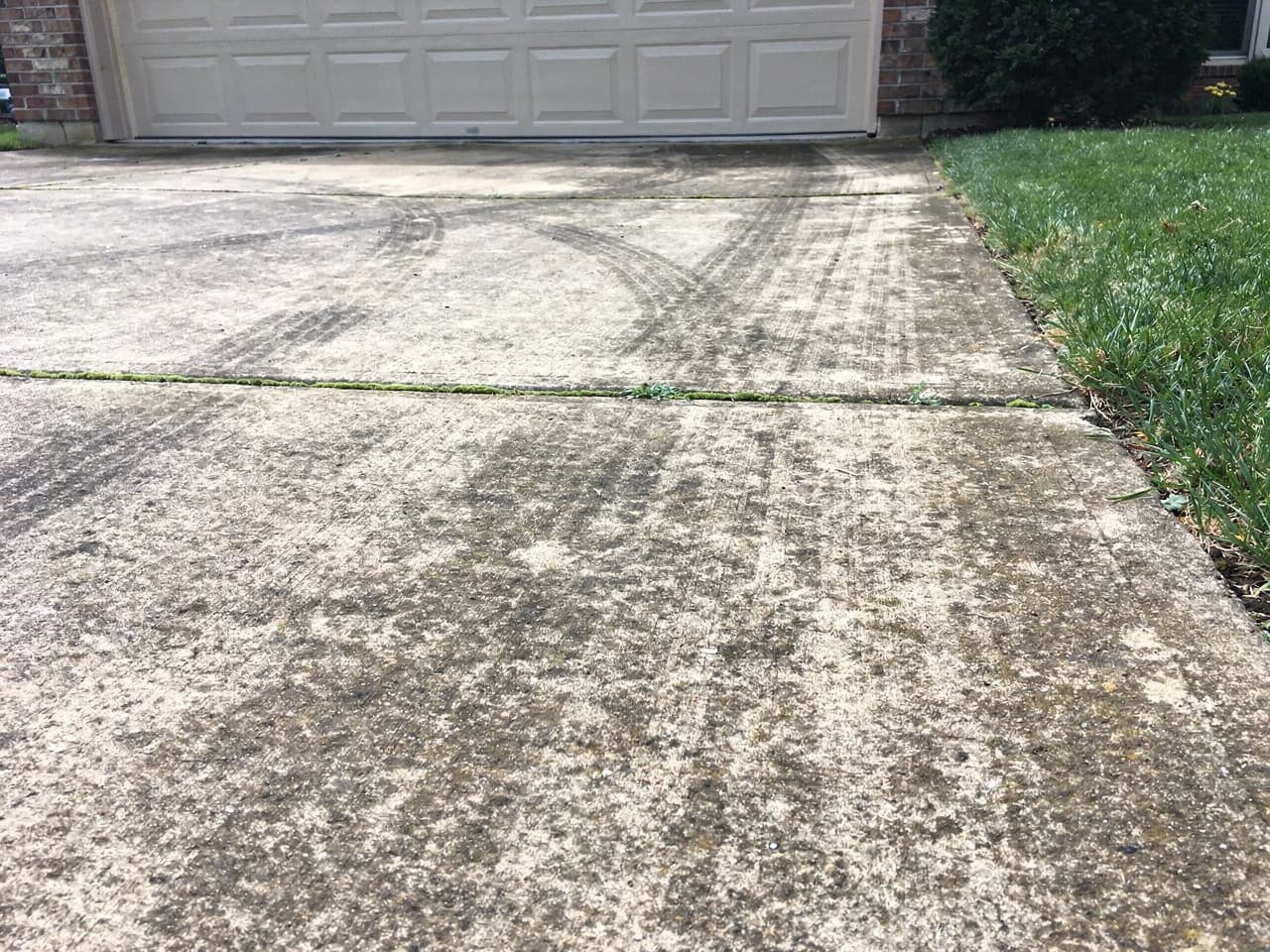 A concrete driveway dulled by grime, tire marks, and moss in the joints