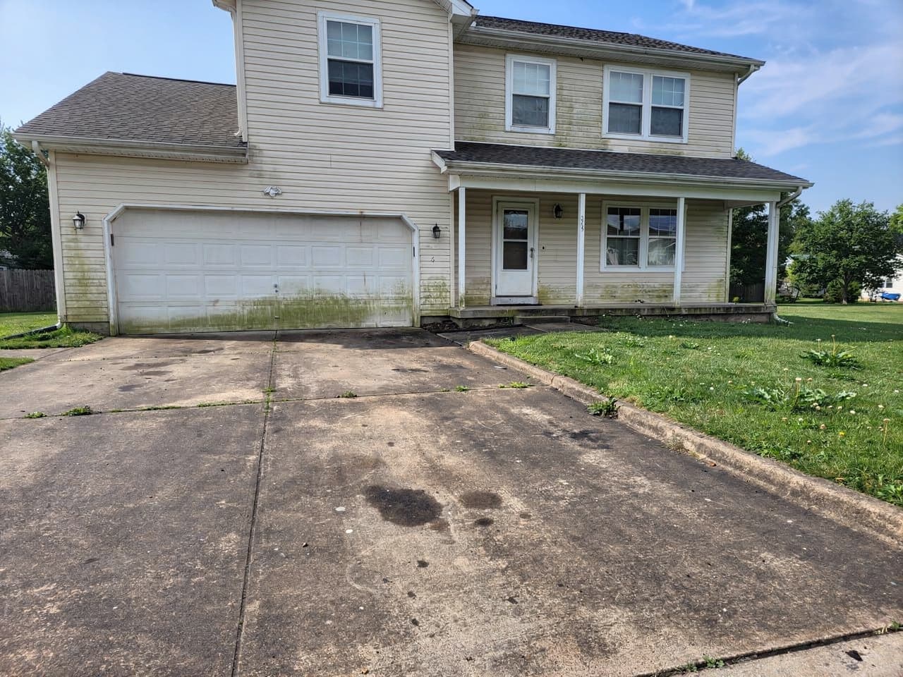 A home with a grimy, tire-marked driveway and dingy siding before washing