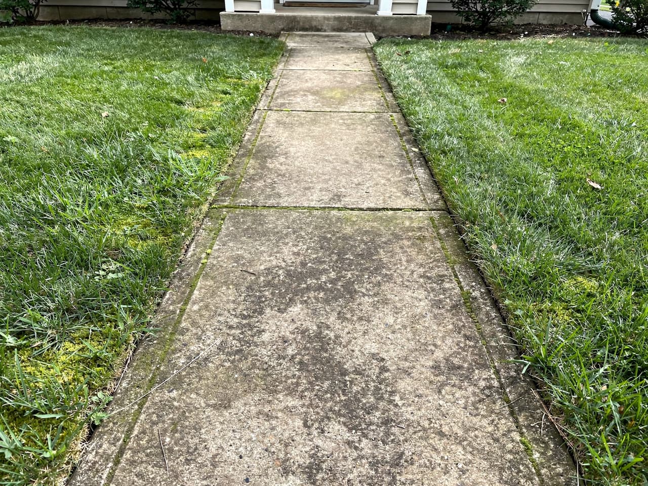 A front walkway grimy and moss-edged before pressure washing